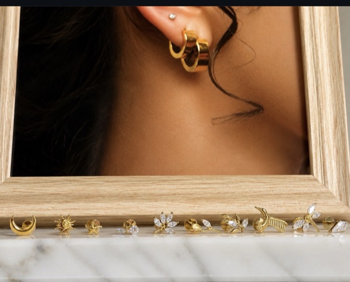 Clous dorés présentés sur du marbre : lune, soleil, étoile, fleurs de marquises et oiseau